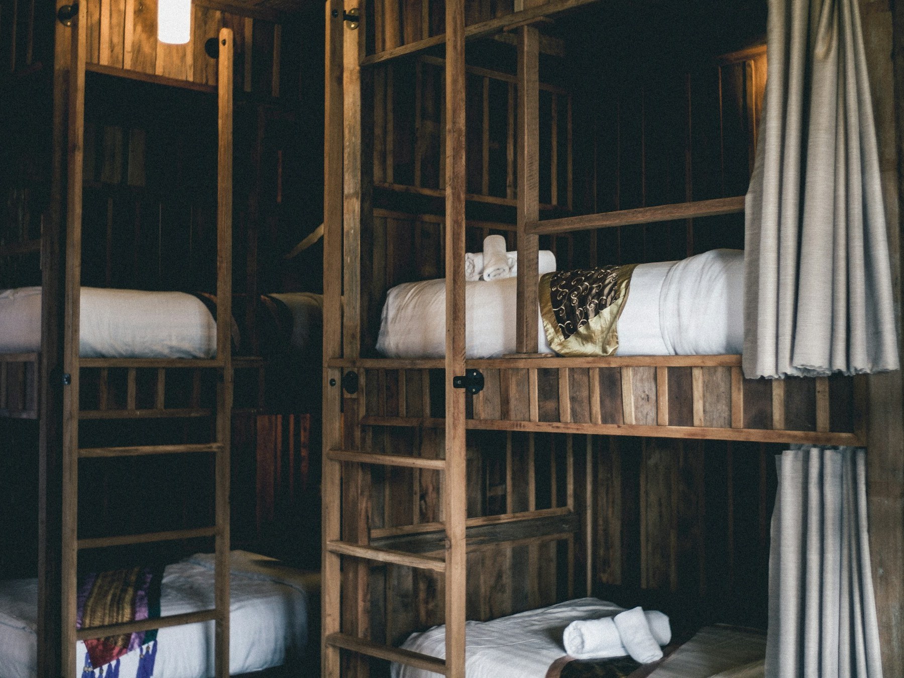 Clean wooden bunk beds with white linen in a hostel dorm room