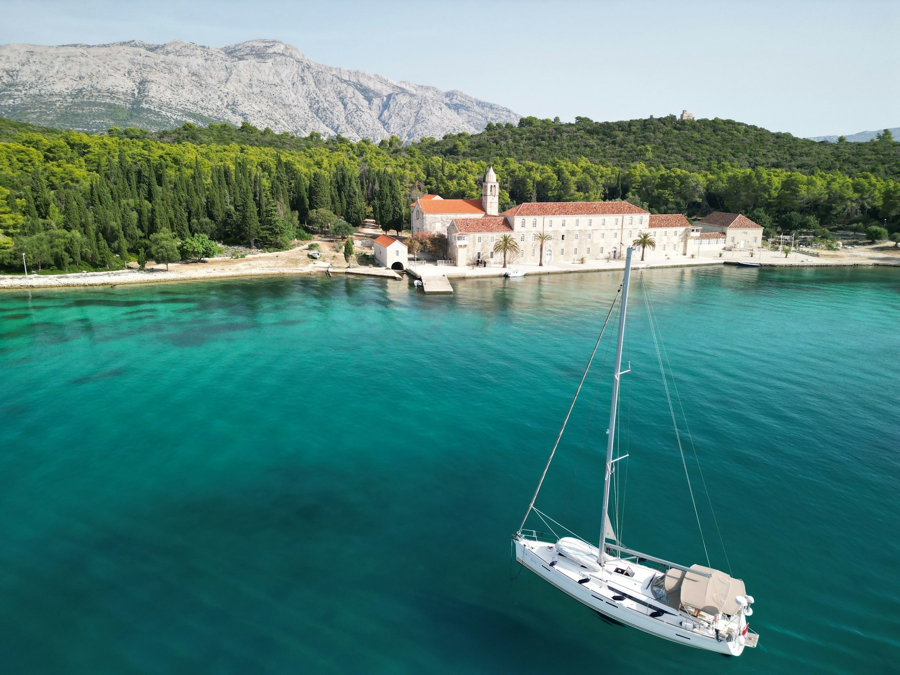 White sailboat anchored in clear turquoise water near a Croatian island shore